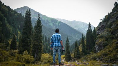 man in blue and white checked quarter sleeved shirt holding black camera standing on rock