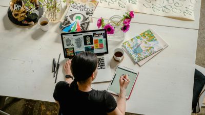 woman writing on tab while using laptop